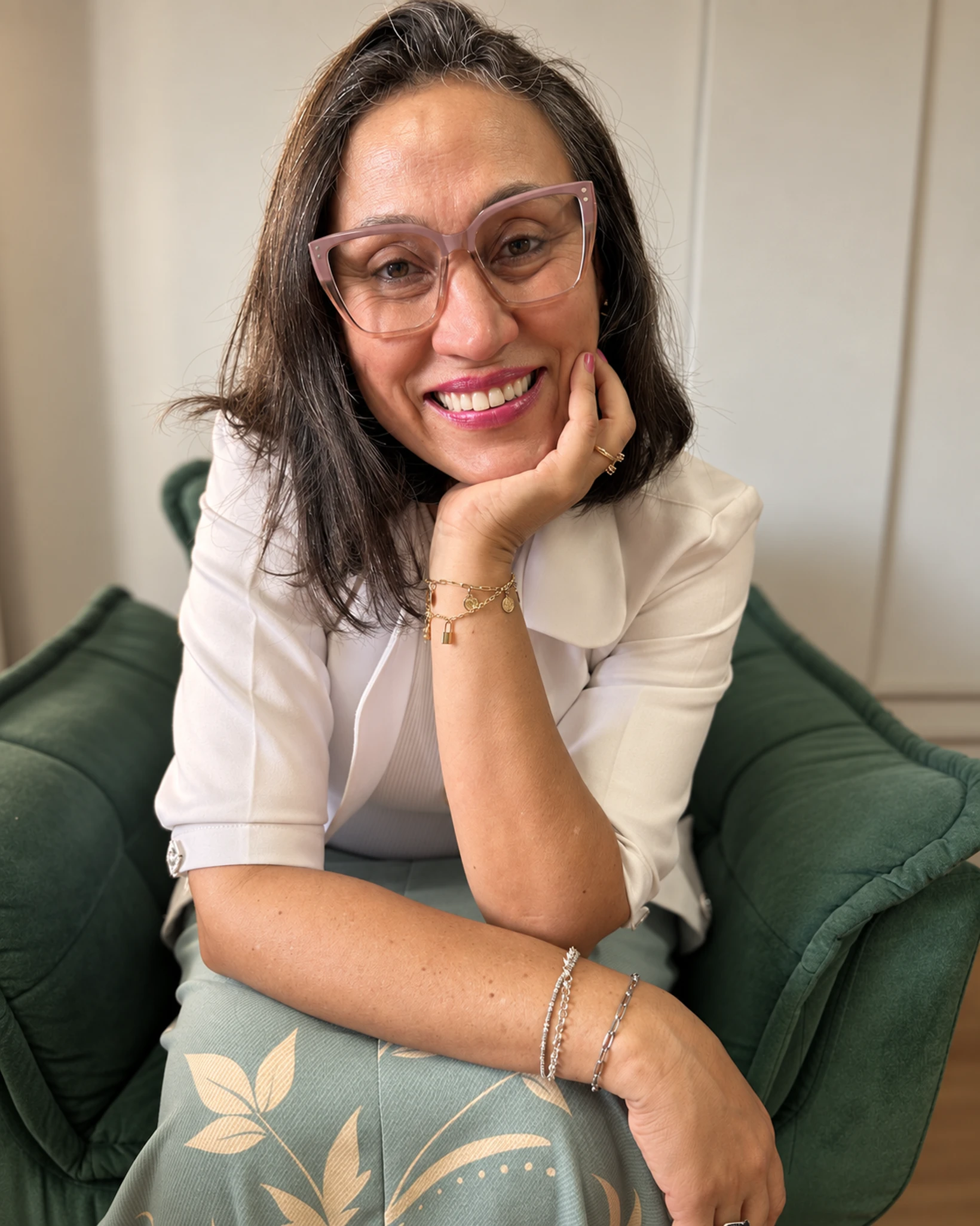Alessandra Muniz sorrindo, sentada na poltrona do seu espaço de atendimento.